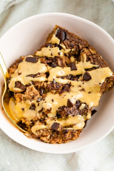 Slice of chocolate baked oatmeal in a bowl drizzled with peanut butter.