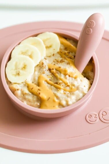 Rolled oats for baby with banana, peanut butter and flaxseed in a ezpz bowl with an ezpz spoon in the oatmeal.