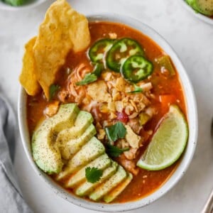 Bowl of chicken tortilla soup with avocado, line, jalapeno and chips as garnish.