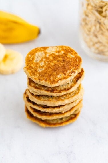 Stack of small pancakes. Banana and oats in the background.