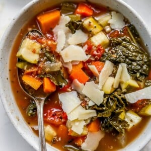 Bowl of quinoa vegetable soup with a spoon lifting some soup out of the bowl.