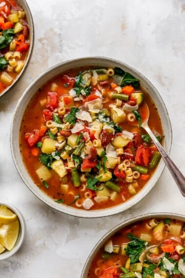 An overhead photo looking at a bowl of minestrone soup. There are two additional bowls cut out of the frame.