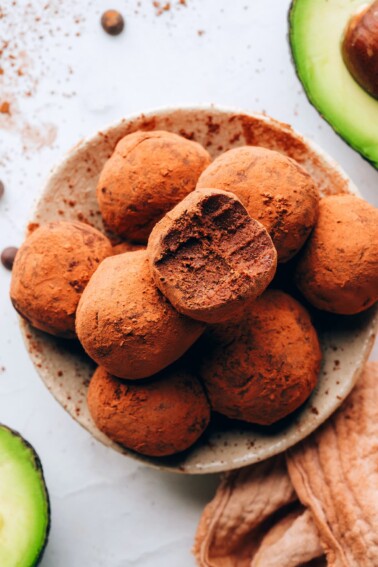 An overhead photo of a bowl of avocado truffles. The top truffle has a bite taken out of it.