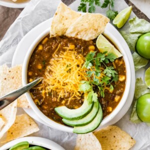 A bowl of vegetarian chili verde served with avocado, lime, cheese, cilantro and a tortilla.