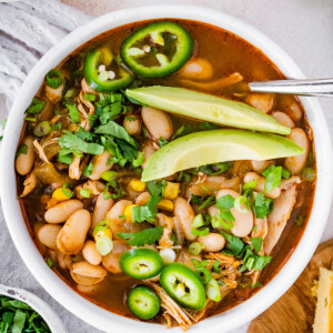 A bowl of white bean chicken chili topped with jalapeño slices and avocado.