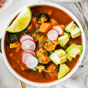 A bowl of Mexican sweet potato chicken soup topped with sliced radish, cilantro, avocado, and a lime wedge.