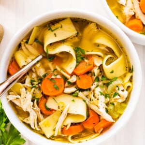 Chicken noodle soup in a white bowl with a metal spoon.