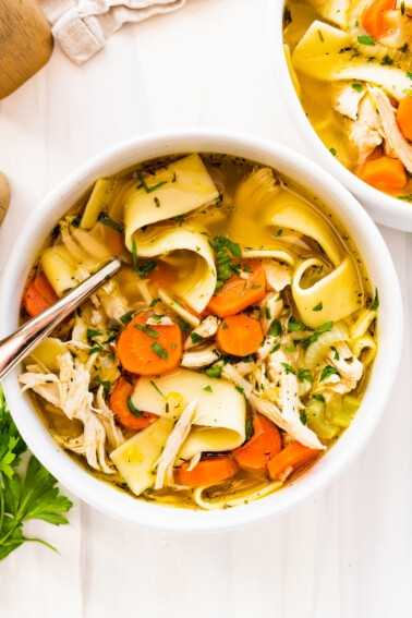 Chicken noodle soup in a white bowl with a metal spoon.