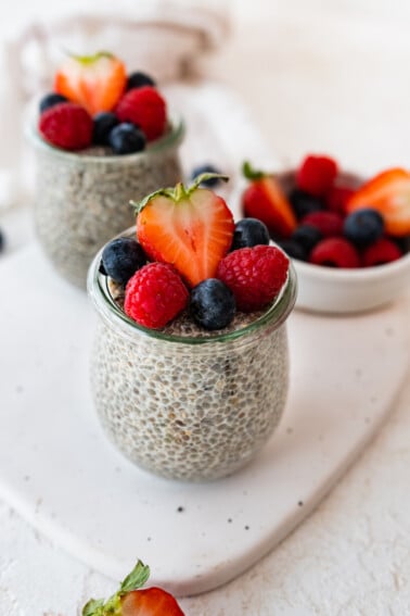 Two glass cups with chia pudding on a table topped with fresh berries.