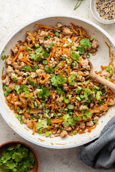 A skillet containing egg roll in a bowl. A wooden serving spoon rests in the pan.