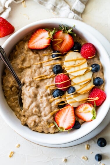 A bowl of protein oatmeal topped with fresh berries, banana slices, and a drizzle of nut butter.