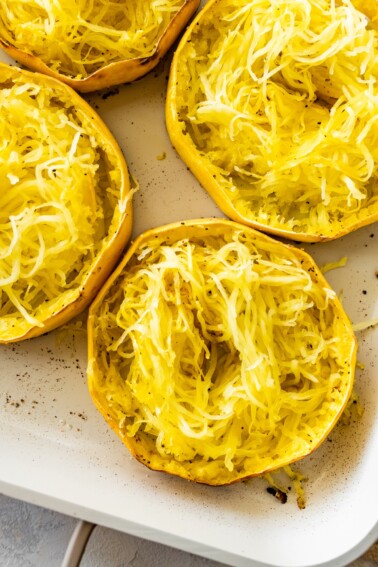 Roasted spaghetti squash rings in a white baking dish. The rings are shredded into long strands.