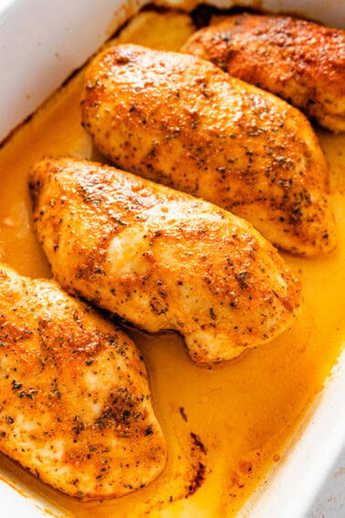 Four baked chicken breasts in a large baking dish.