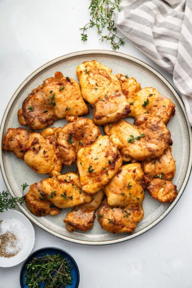 Baked boneless chicken thighs on a plate, garnished with fresh herbs.