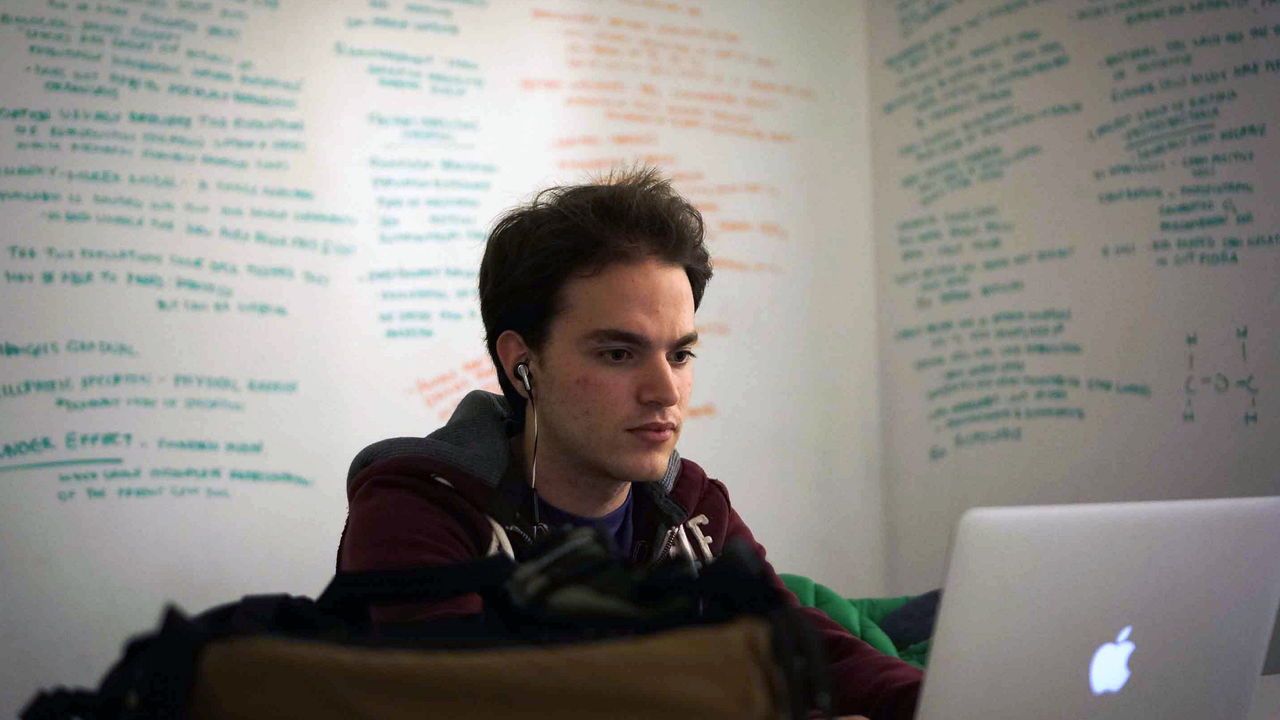 A student studies on his laptop with notes covering whiteboards.