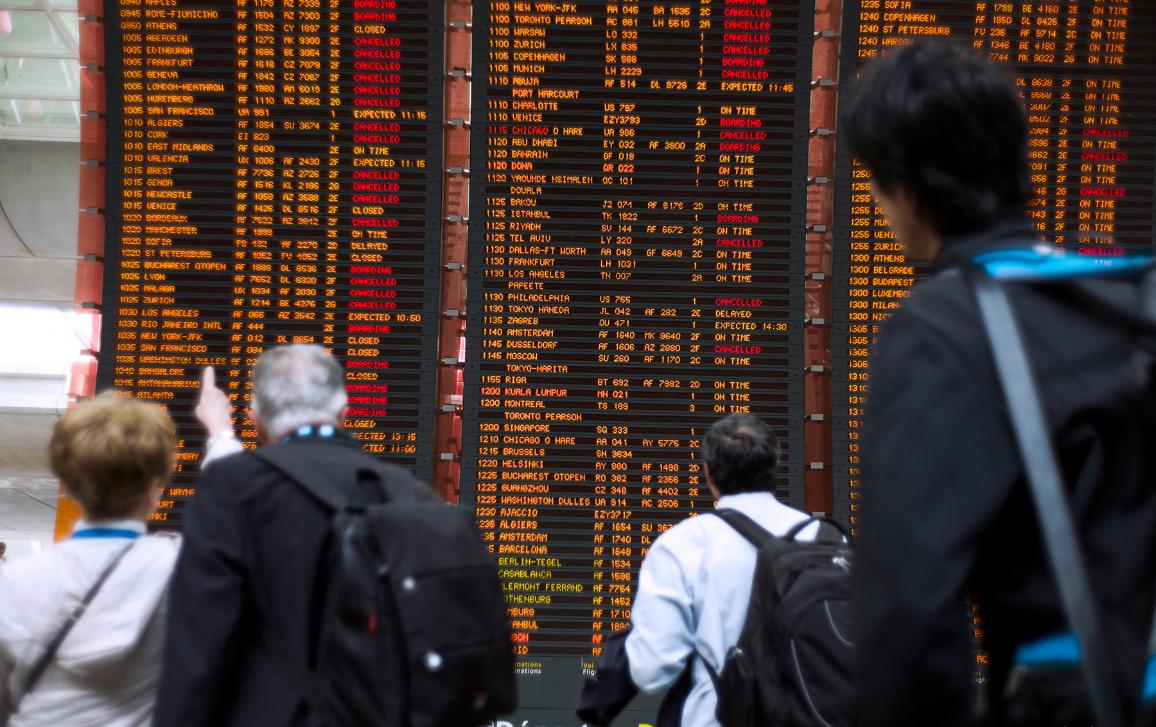 Os viajantes verificam um quadro que mostra os voos cancelados desde o aeroporto internacional Roissy Charles de Gaulle, fora de Paris.