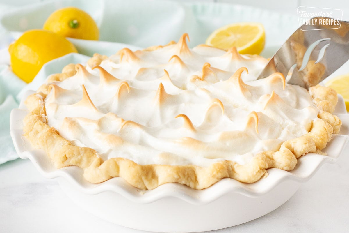 Serving spatula slicing into a baked whole Lemon Meringue Pie.