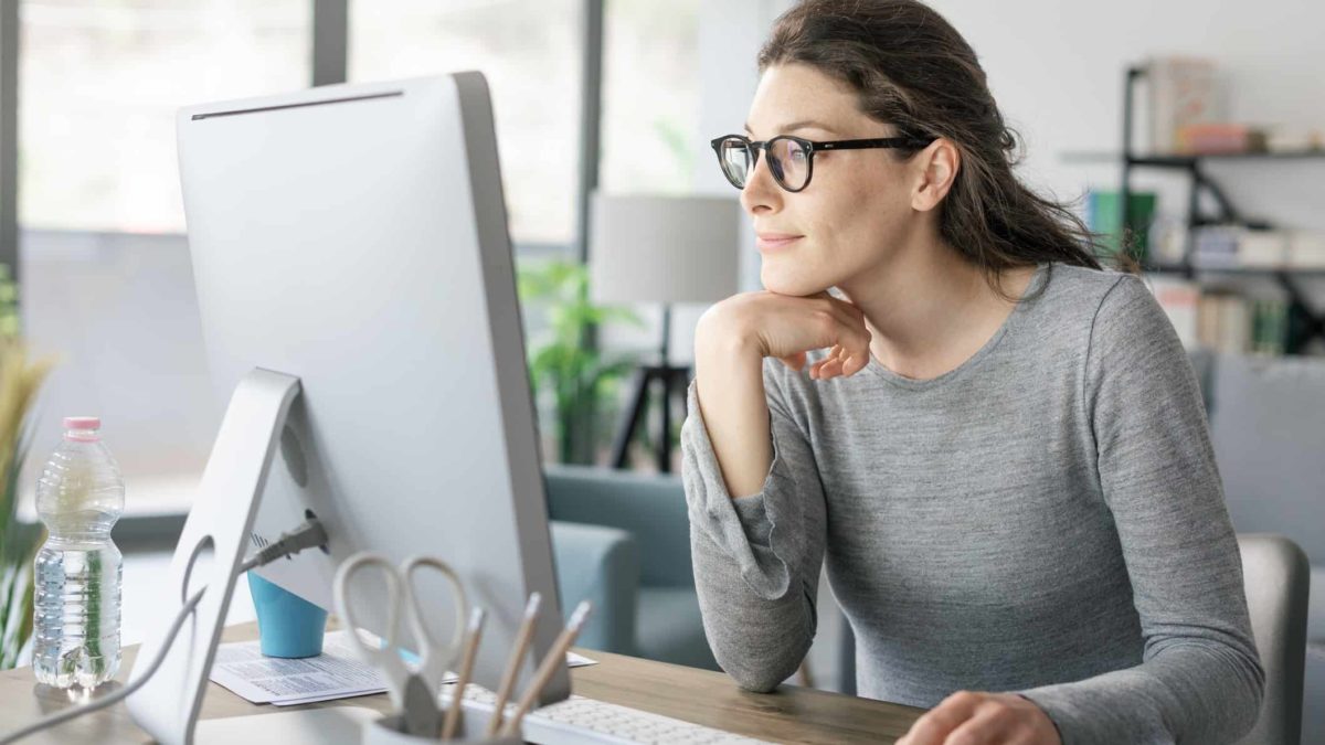 A woman sits at her computer with her chin resting on her hand as she contemplates her next potential investment.