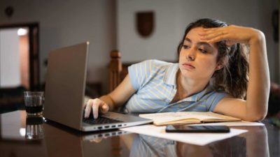 A young woman slumped in her chair while looking at her laptop.