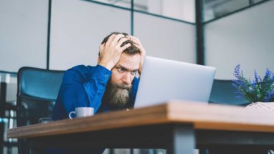 A man holds his head in his hands, despairing at the bad result he's reading on his computer.