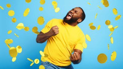 A man clenches his fists in excitement as gold coins fall from the sky.