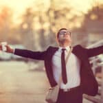 Businessman smiles with arms outstretched after receiving good news.