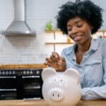 Woman at home saving money in a piggybank and smiling.