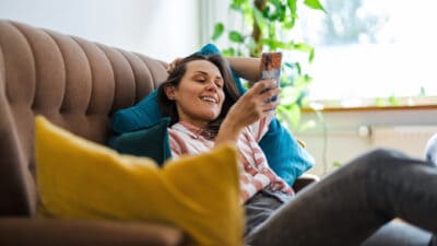 Woman relaxing on her phone on her couch, symbolising passive income.