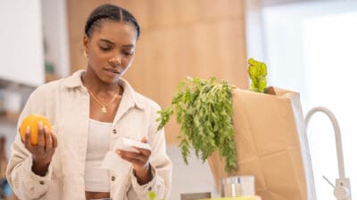 Woman holding an orange and looking at the expensive grocery receipt, symbolising inflation.