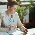 Modern accountant woman in a light business suit in modern green office with documents and laptop.