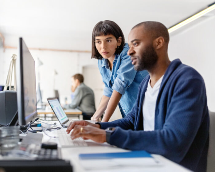 a woman looks over a man's shoulder at his computer as they work out a problem