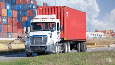 A white truck pulling a red ocean container at the Port of Houston