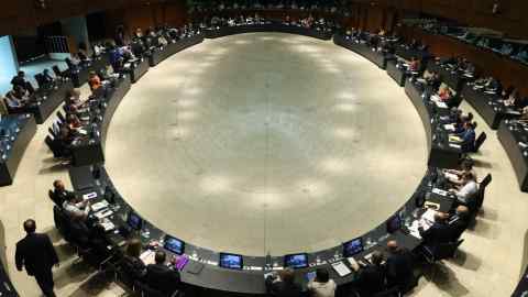 Politicians sits at a very large circular table in a large hall