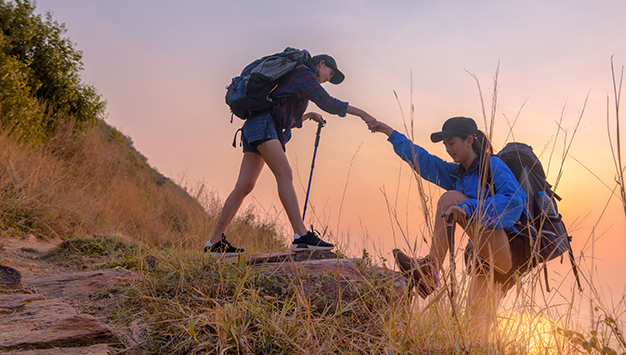 Two asian female hikers climbing up silhouette mountain cliff . helping ,helps and team work concept.