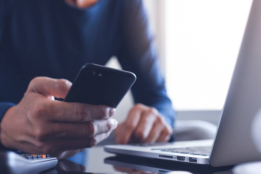 Person reviewing information on their smartphone and laptop at the same time.