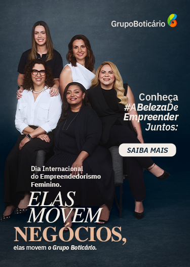 Na imagem do banner, em um fundo preto, iluminado no centro, temos cinco mulheres lado a lado, sorrindo e posando para a câmera. Da esquerda para a direita, a primeira mulher está em pé. Ela é branca de olhos castanho-escuros e cabelos lisos e castanhos, veste uma camiseta preta e usa um relógio preto no punho esquerdo. Na frente dela, temos a segunda mulher, que está sentada. Ela é uma mulher madura, branca, de olhos castanho-escuros e cabelos encaracolados pretos, na altura dos ombros. Ela veste uma camisa branca, uma calça preta e um sapato de bico fino preto com pontos metálicos. Ela usa um colar de pérolas brancas, um relógio no punho esquerdo e óculos de grau de armação marrom. Em pé, ao lado da primeira mulher, temos a terceira. Ela é uma mulher madura, branca, de olhos e cabelos castanho-escuros. Ela veste uma regata branca de um ombro só. Na frente dela, sentada, temos a quarta mulher. Ela é negra de olhos castanho-escuros e cabelos lisos e pretos. Ela veste uma blusa preta sobreposta por um cardigan preto, uma calça preta e sapatos pretos e abertos de salto baixo e usa um colar dourado. Ao lado dela, temos a última. Ela é uma mulher madura, branca, de olhos castanho-escuros e cabelos loiros ondulados. Ela veste uma blusa preta sobreposta por um colete preto, uma calça preta e sapatos scarpin pretos. À esquerda da imagem, no canto inferior, em letras beges e na cor salmão, o texto: “Dia Internacional do Empreendedorismo Feminino. Elas movem negócios, elas movem o Grupo Boticário.”. À direita, em letras bege e uma caixinha bege com letras azul-escuras, os textos: “Conheça #ABelezaDeEmpreenderJuntos:” e “Saiba mais”. Logo do Grupo Boticário no canto superior direito.