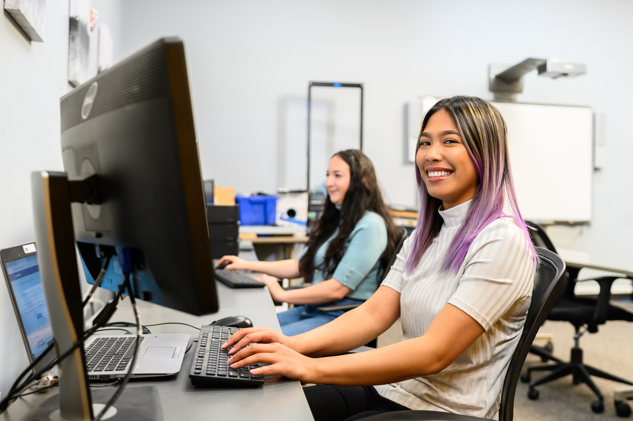 Two women sitting in front of computers typing