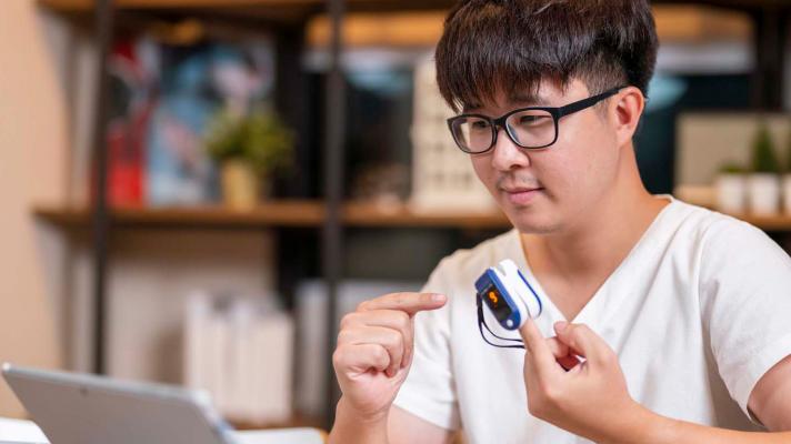 Person in front of laptop with remote medical device on finger