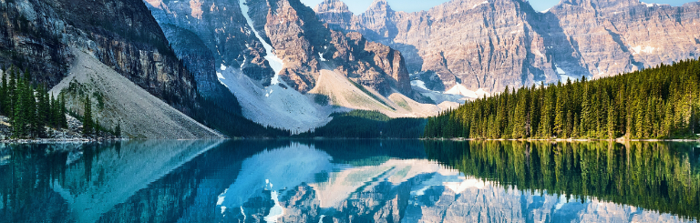 Moraine Lake with steep mountains on the left, rows of pine trees on the right, and everything reflected in the lake in the center.