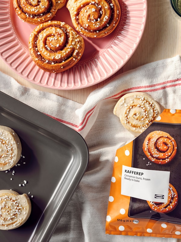 A bag of KAFFEREP cinnamon buns is open and there are two unbaked buns on a baking tray and three baked ones on a plate.