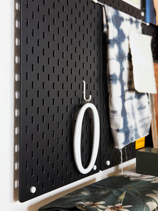 Side-by-side, wall-mounted black SKÅDIS pegboards with pieces of fabric and other decorative items attached to them.