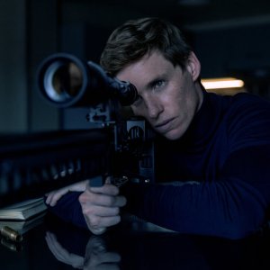 THE DAY OF THE JACKAL stars Eddie Redmayne as the Jackal, shown here wearing a blue turtleneck looking through a sniper rifle scope