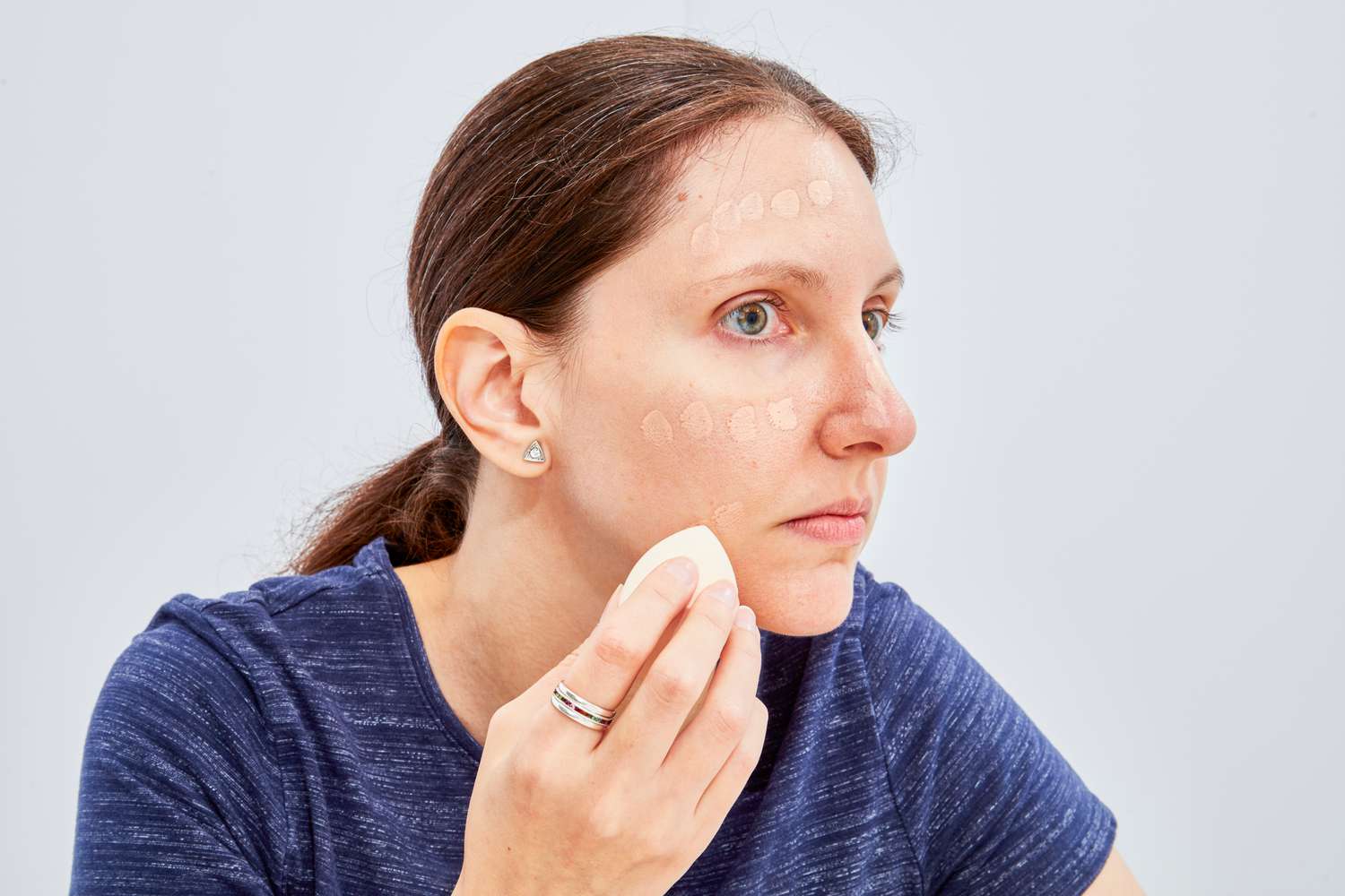 A person using a sponge to blend dots of Giorgio Armani Beauty Luminous Silk Foundation into their cheek