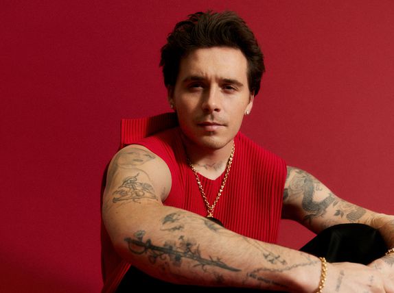 Brooklyn Beckham sitting in a red tank top and black pants