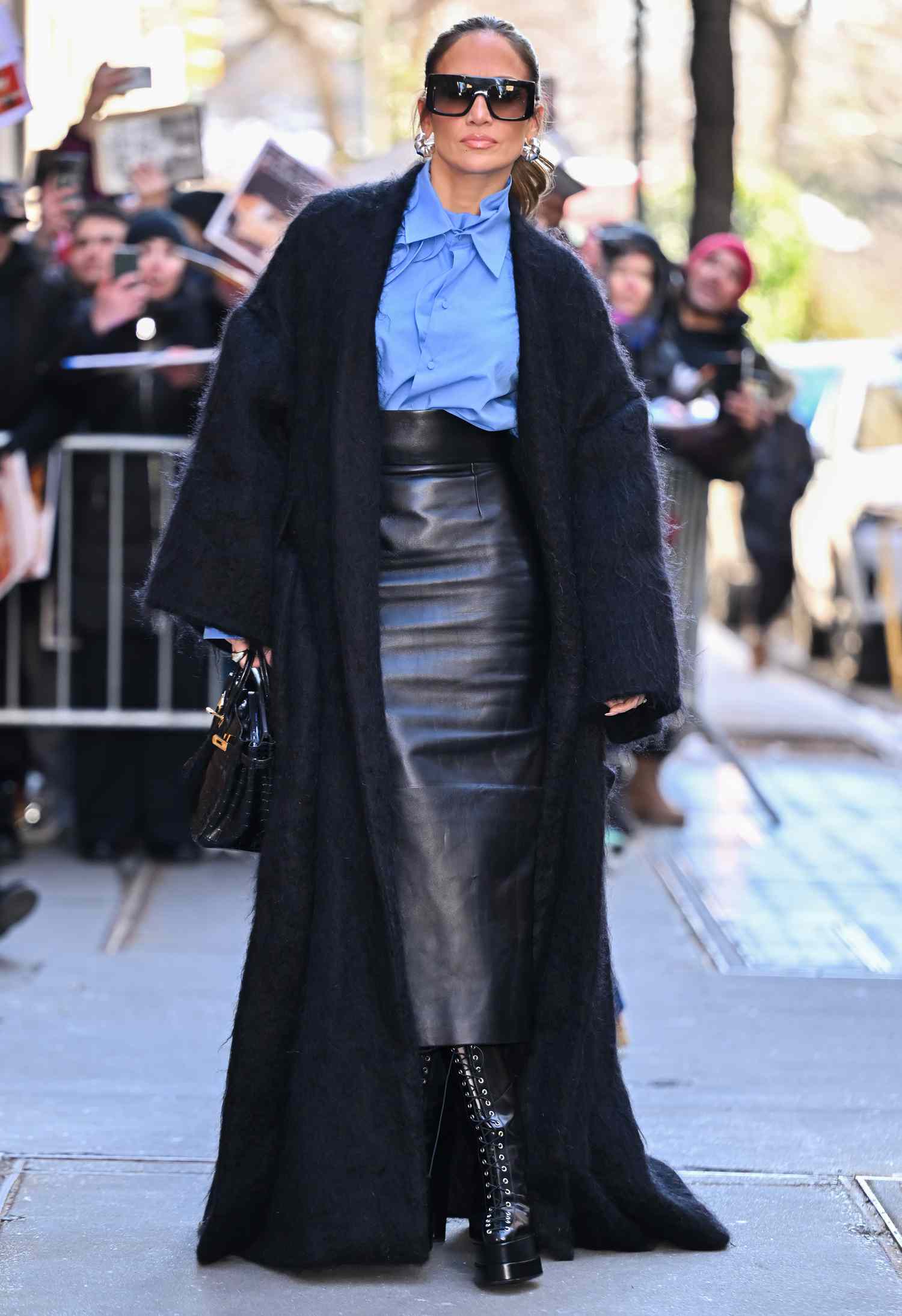 Jennifer Lopez photographed wearing a blue button up, black leather skirt, and black coat