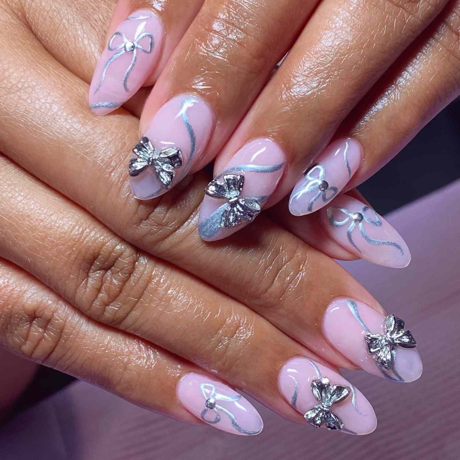 close up of nails with light pink manicure with silver bows