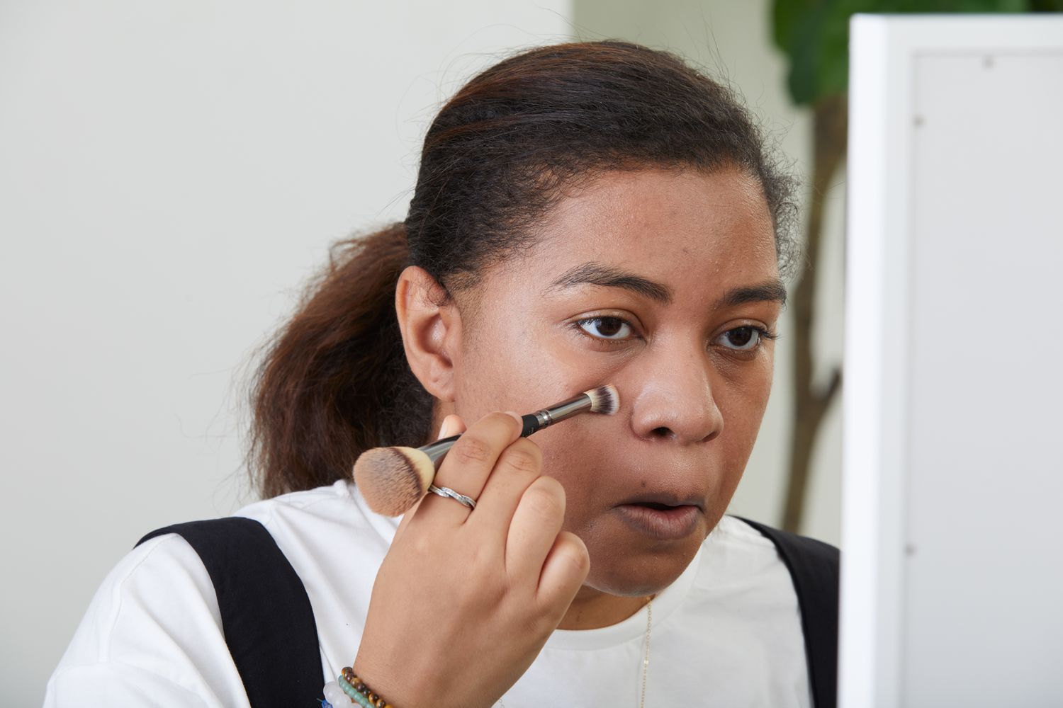 Person applying Tower 28 SunnyDays SPF 30 Tinted Sunscreen with cosmetic brush while looking into mirror