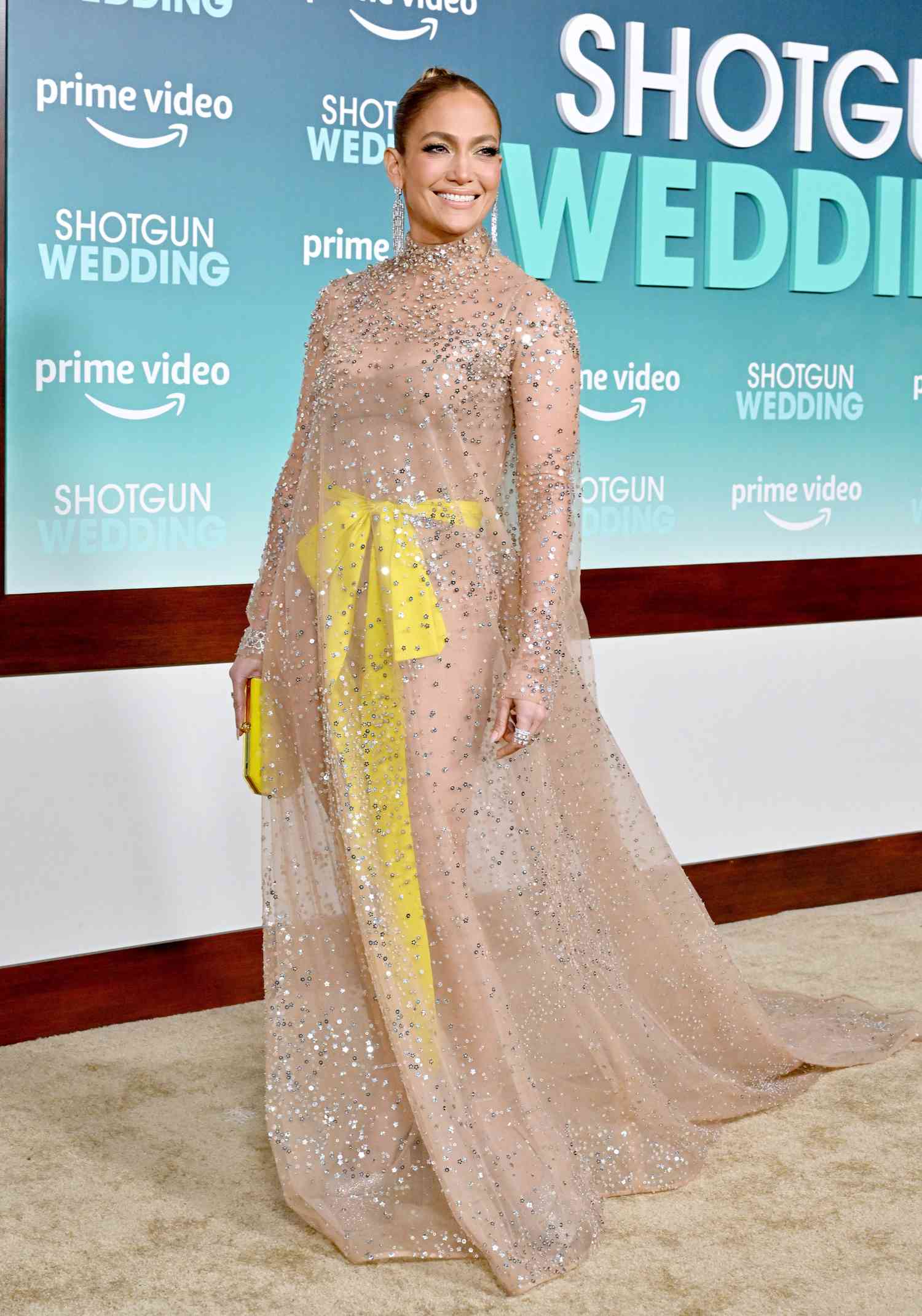 Jennifer Lopez wearing a nude sheer gown with yellow sash and sparkly details