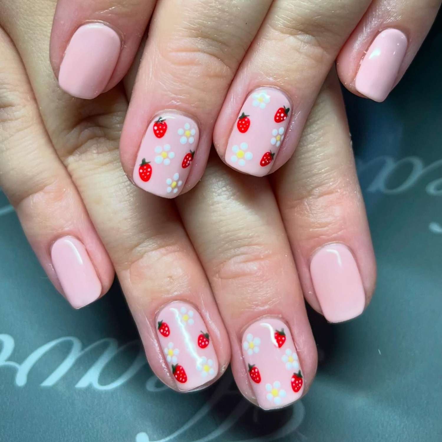 close up of nails with light pink manicure with hand painted flowers and strawberries