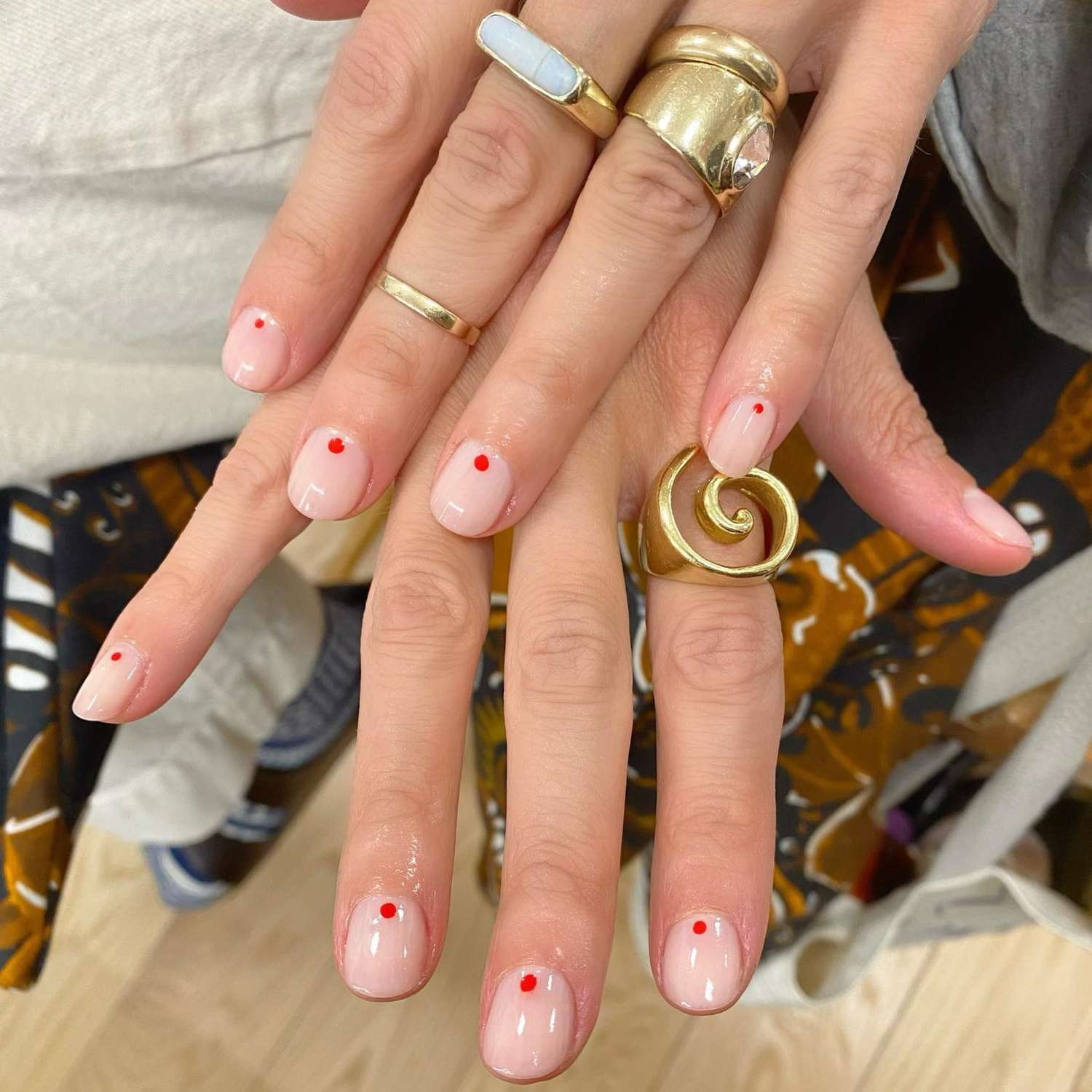 close up of nails with light pink manicure with one red tiny dot on each nail